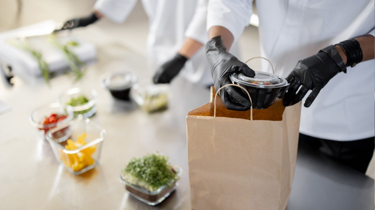 Photo of someone putting pots of food in a paper bag
