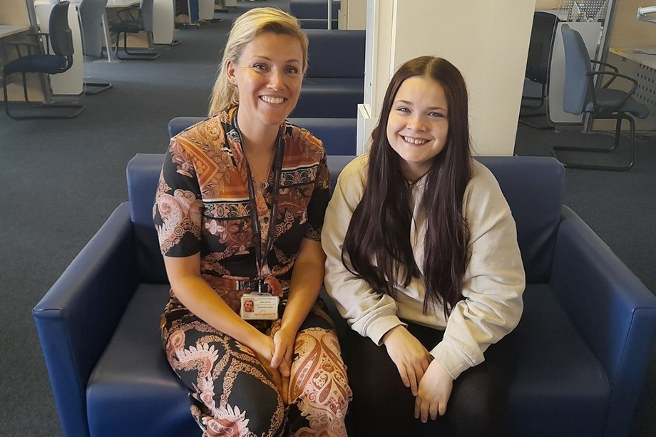 Photo of two people sat on a sofa, smiling at the camera